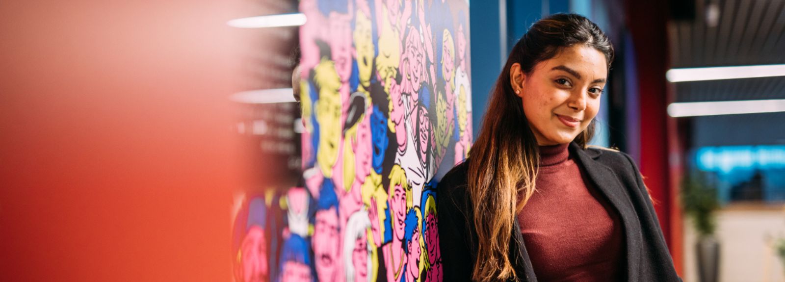 female student standing smiling to camera at a colourful wall